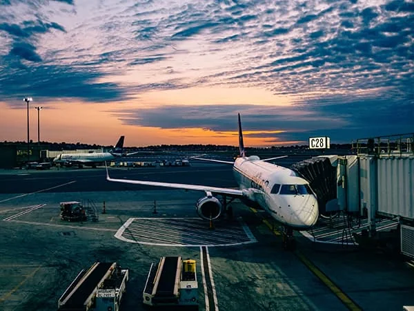 Un avion stationné au pied d’une passerelle d’aéroport au coucher du soleil.