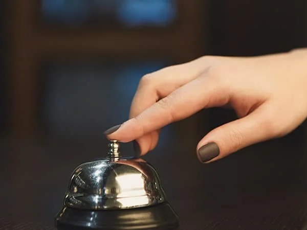 Une main appuie sur la sonnette d’un comptoir d’accueil.