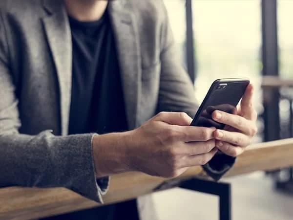 Une personne en veste grise utilise un téléphone portable, accoudée à un comptoir en bois.
