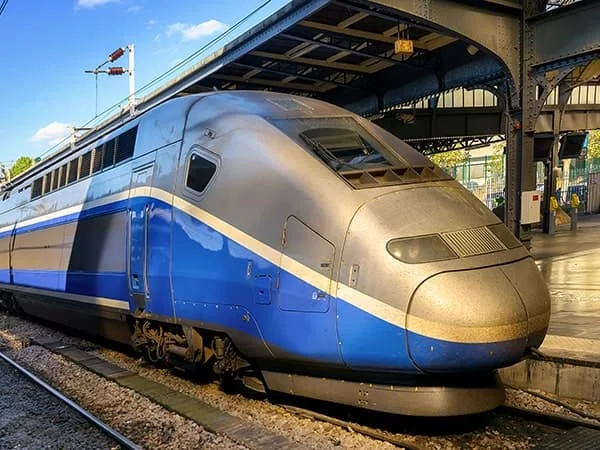 Un train à grande vitesse bleu et gris à quai sous la verrière d’une gare.