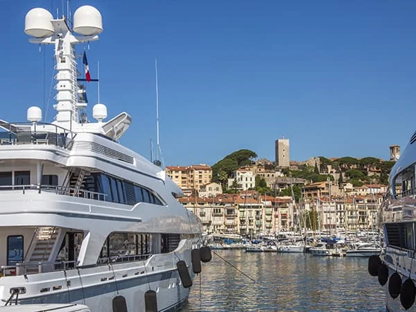 Des yachts amarrés dans un port, avec des immeubles et une tour sur la colline en arrière-plan.